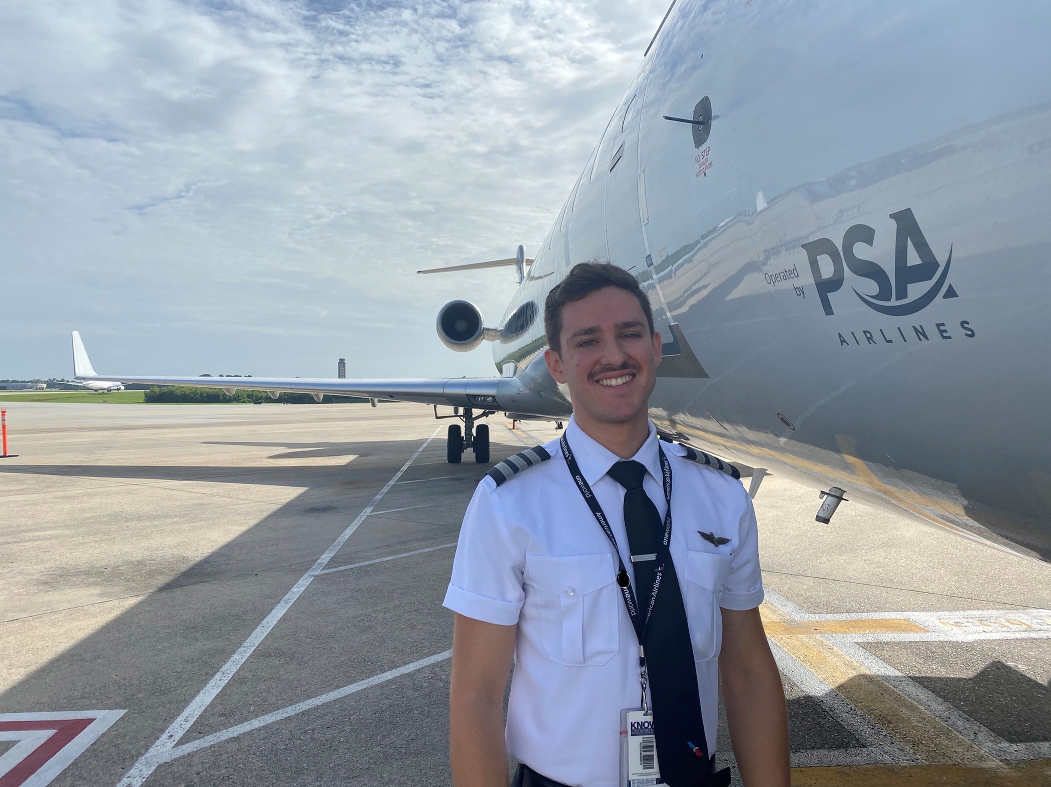 First Officer Adam Sciupac outside standing on the side of PSA aircraft smiling
